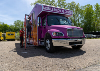 Exterior of purple Mobile Medical Center unit with 2 men working on it.