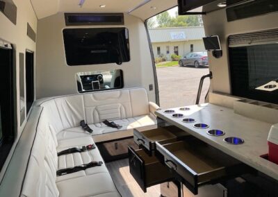 Interior of indulger specialty vehicle showing back end view of kitchenette, TV, and bench seating with door open.