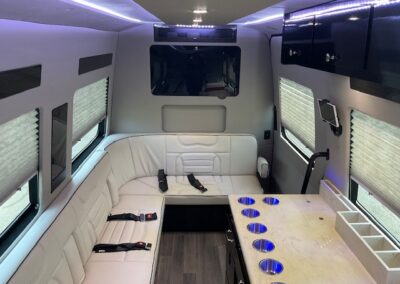 Interior of indulger specialty vehicle showing long white L shaped bench, countertop with several cup holders, and TV.