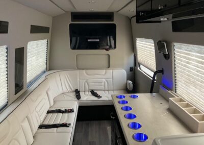 Interior of indulger specialty vehicle showing long white L shaped bench, countertop with several cup holders, and TV.