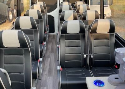 Front to back view of interior of pano specialty vehicle showing beverage center on right and 13 black and tan leather seats.