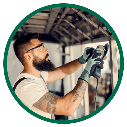 Round image with green outside circle showing man in white shirt with safety glasses and gloves on holding tool refurbishing metal products.