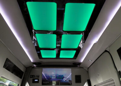 Interior of TWR specialty vehicle with six green overhead lights on ceiling, overhead white lights on the sides, and tv screen in the front.