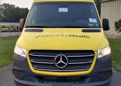 Front end exterior view of a yellow Mercedes-Benz mobile marketing vehicle with MetroPlusHealth logo.