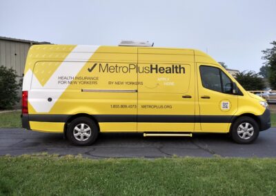 Passenger side exterior view of a yellow Mercedes-Benz mobile marketing vehicle with MetroPlusHealth logo. "Health Insurance for New Yorkers" "By New Yorkers" "Apply Here" "1.855.809.4073" "metroplus.org"