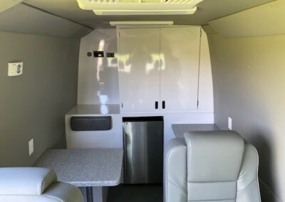 Back end interior view of a mobile marketing specialty vehicle Image shows a choir, table, shelve, and cabinets.