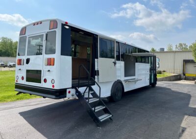 Exterior image of a white Outreach Mobile Meal Dispensing specialty vehicle. Back end has stairs coming down from vehicle, middle has an open window with shelf for serving.