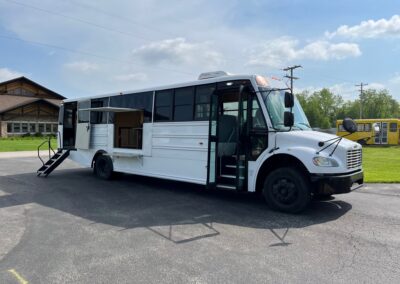 Exterior image of a white Outreach Mobile Meal Dispensing specialty vehicle. Back end has stairs coming down from vehicle, middle has an open window with shelf for serving.