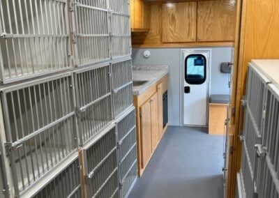 Back end interior image of pet services specialty vehicle showing kennels on each side and cabinets.