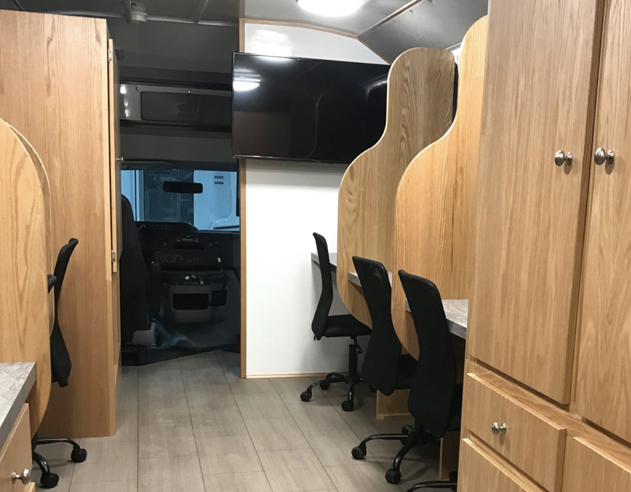 Dark image of 2 office chairs pulled under a desk with man sitting in the background.
